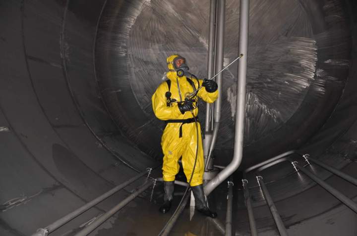 Un technicien en équipement de protection individuelle effectuant le ramonage des conduits dune chaudière industrielle, dans un environnement propre.